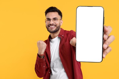Happy man holding smartphone with empty screen on orange background, space for text