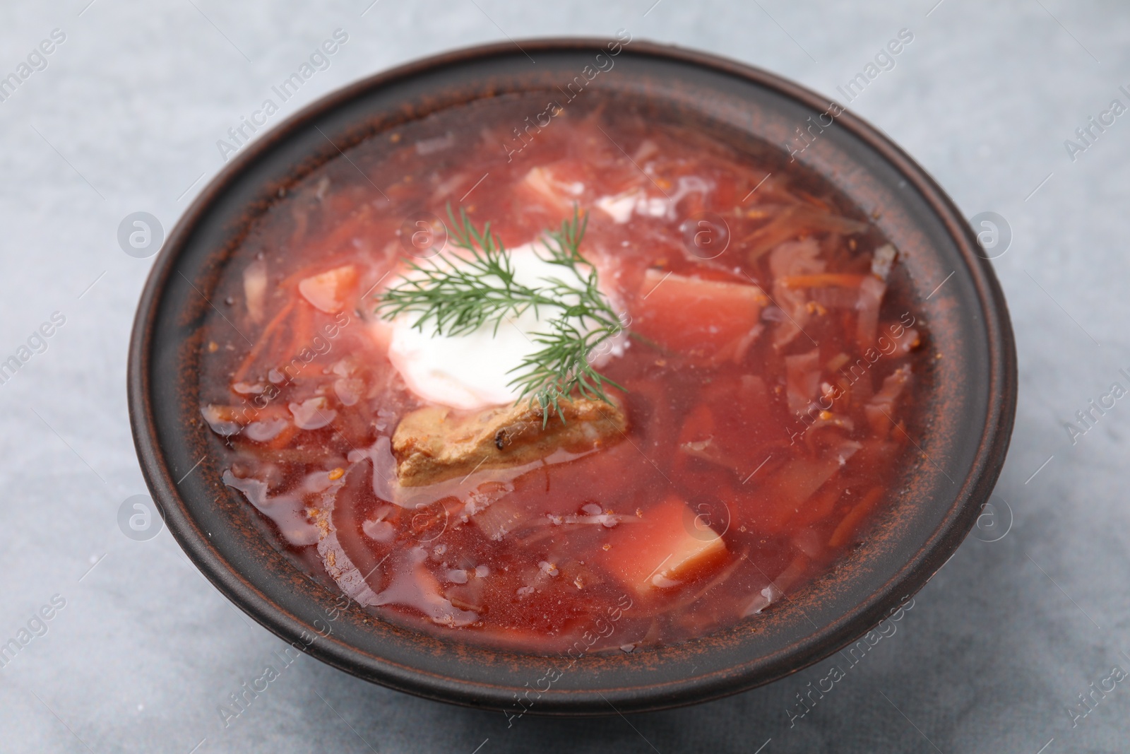 Photo of Tasty borscht with sour cream in bowl on light grey table, closeup