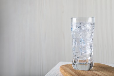 Photo of Glass of soda water with ice on white wooden table. Space for text