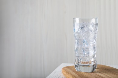 Glass of soda water with ice on white wooden table. Space for text