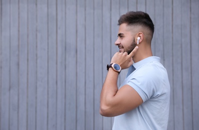 Photo of Young man with wireless headphones listening to music near grey wall. Space for text