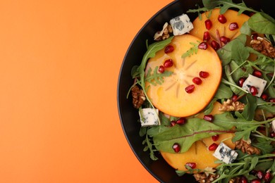 Photo of Tasty salad with persimmon, blue cheese, pomegranate and walnuts on orange background top view. Space for text