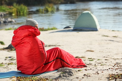 Photo of Man in sleeping bag on wild beach. Space for text