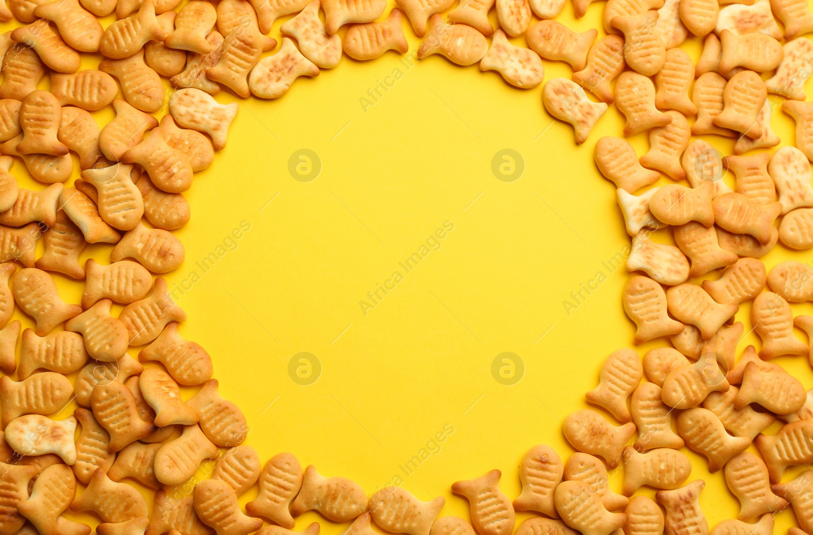 Photo of Frame of delicious goldfish crackers on yellow background, flat lay. Space for text