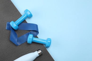 Photo of Two dumbbells, yoga mat, fitness elastic band and thermo bottle on light blue background, flat lay. Space for text