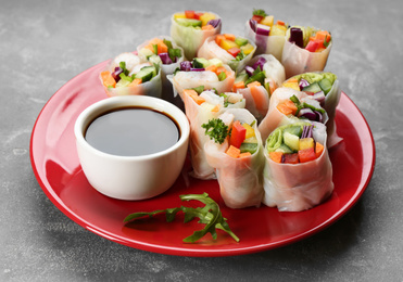 Photo of Delicious rolls wrapped in rice paper served on grey table