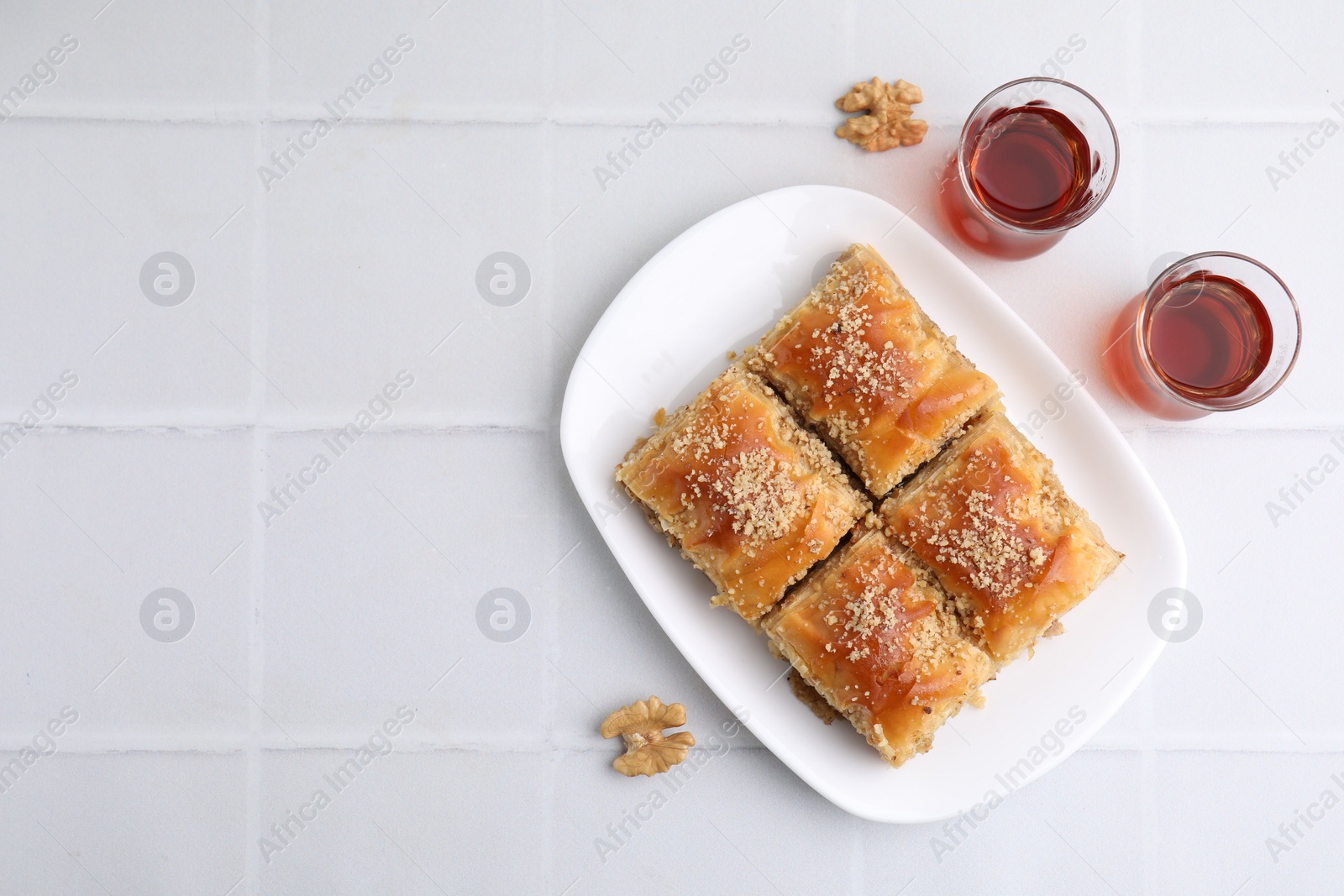 Photo of Eastern sweets. Pieces of tasty baklava, walnuts and tea on white tiled table, flat lay. Space for text