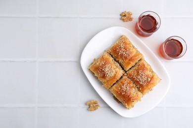 Photo of Eastern sweets. Pieces of tasty baklava, walnuts and tea on white tiled table, flat lay. Space for text