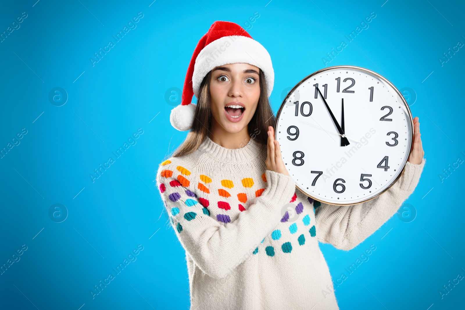 Photo of Woman in Santa hat with clock on light blue background. New Year countdown