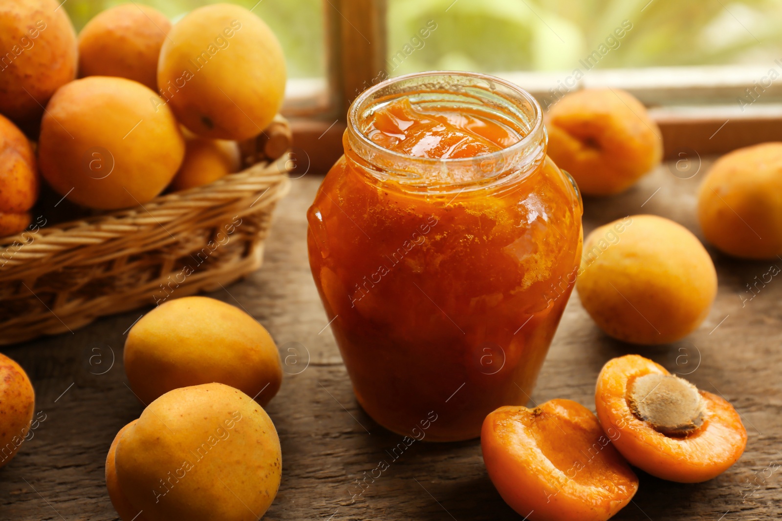 Photo of Jar of delicious jam and fresh ripe apricots on wooden table indoors. Fruit preserve