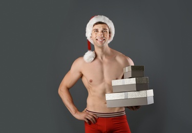 Photo of Young muscular man in Santa hat with gift boxes on gray background