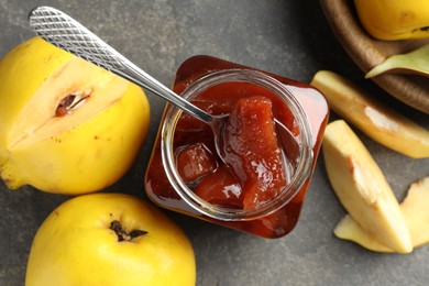 Photo of Tasty homemade quince jam in jar, spoon and fruits on grey textured table, flat lay