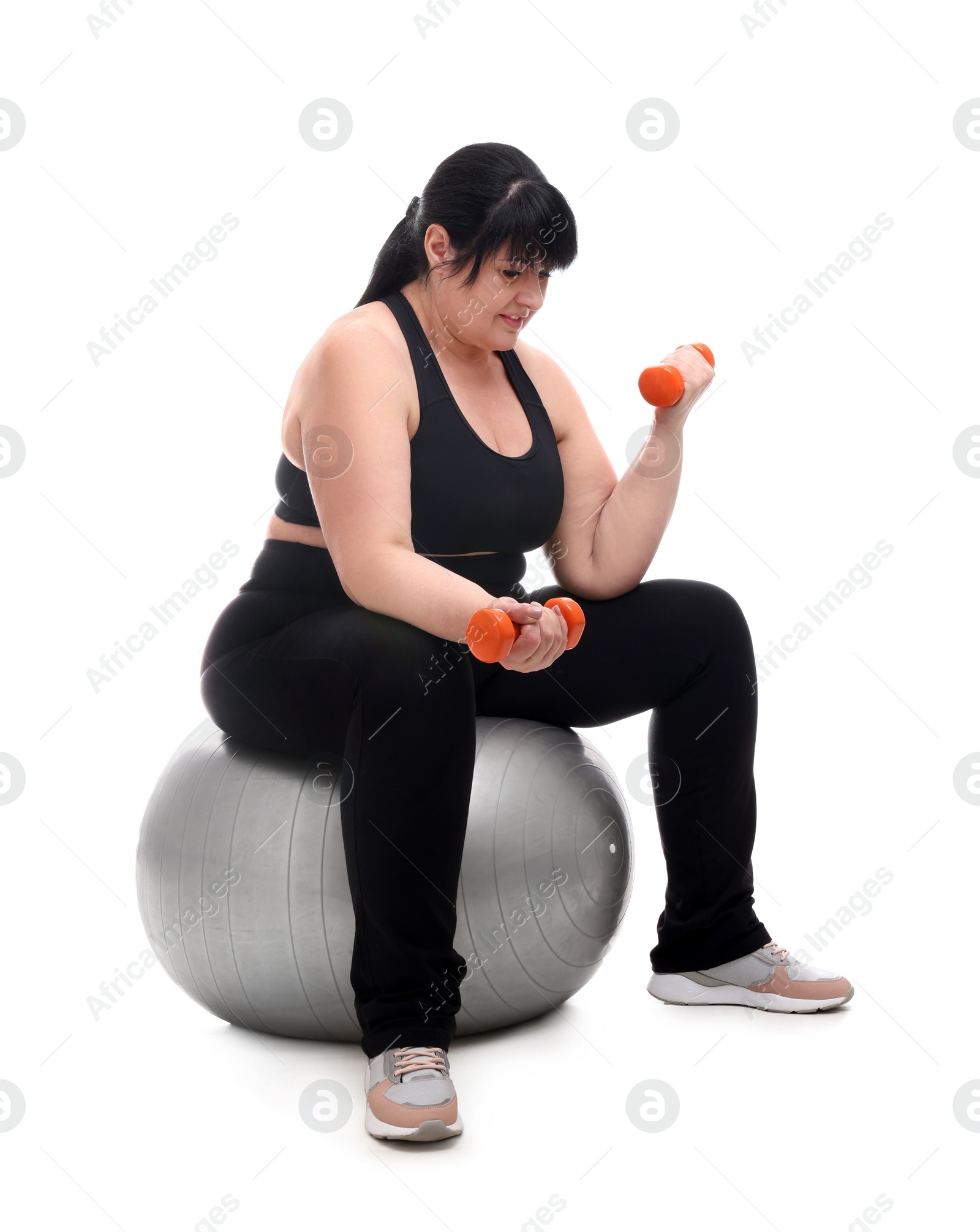 Photo of Happy overweight mature woman with dumbbells sitting on fitness ball against white background