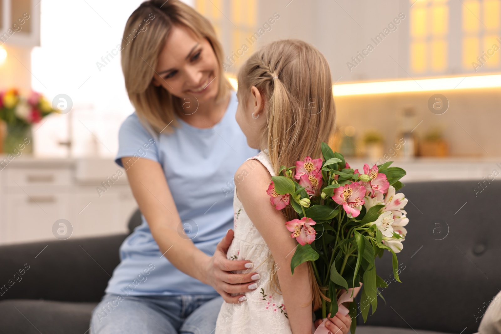 Photo of Little girl hiding bouquet of alstroemeria flowers for mom at home, selective focus. Happy Mother's Day