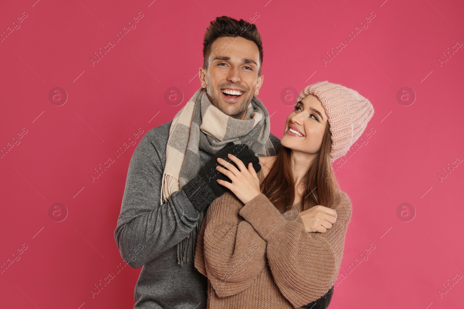 Photo of Happy young couple in warm clothes on pink background. Winter season