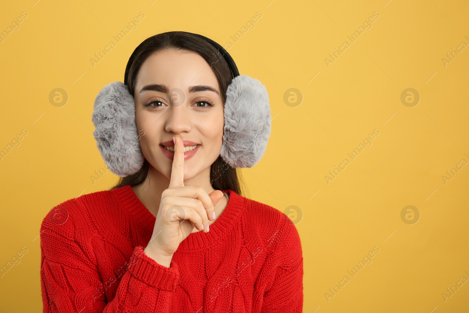 Photo of Beautiful young woman wearing earmuffs on yellow background. Space for text