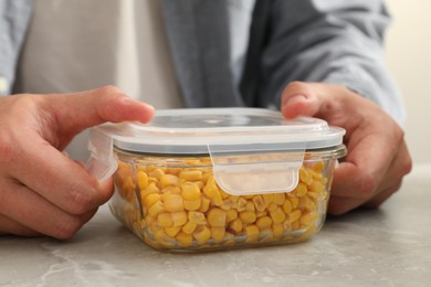 Photo of Man closing glass container with lid at light grey marble table in kitchen, closeup. Food storage