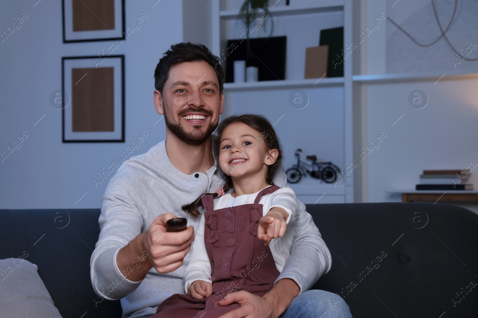 Photo of Happy father and daughter at home. Man changing TV channels with remote control