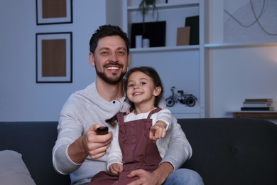 Photo of Happy father and daughter at home. Man changing TV channels with remote control