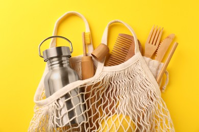Photo of Fishnet bag with different items on yellow background, top view. Conscious consumption