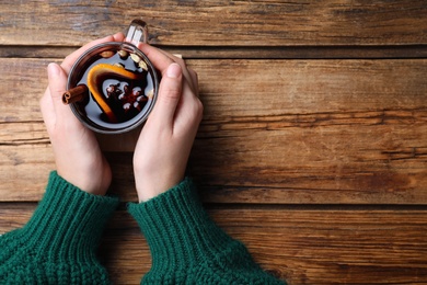 Photo of Woman with cup of mulled wine at wooden table, top view. Space for text