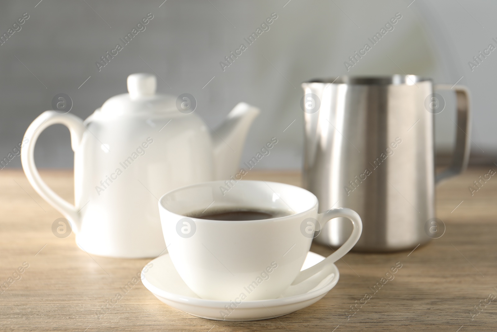 Photo of Aromatic tea in cup, teapot and pitcher on wooden table