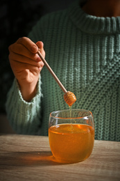 Woman holding honey dipper over jar at wooden table, closeup