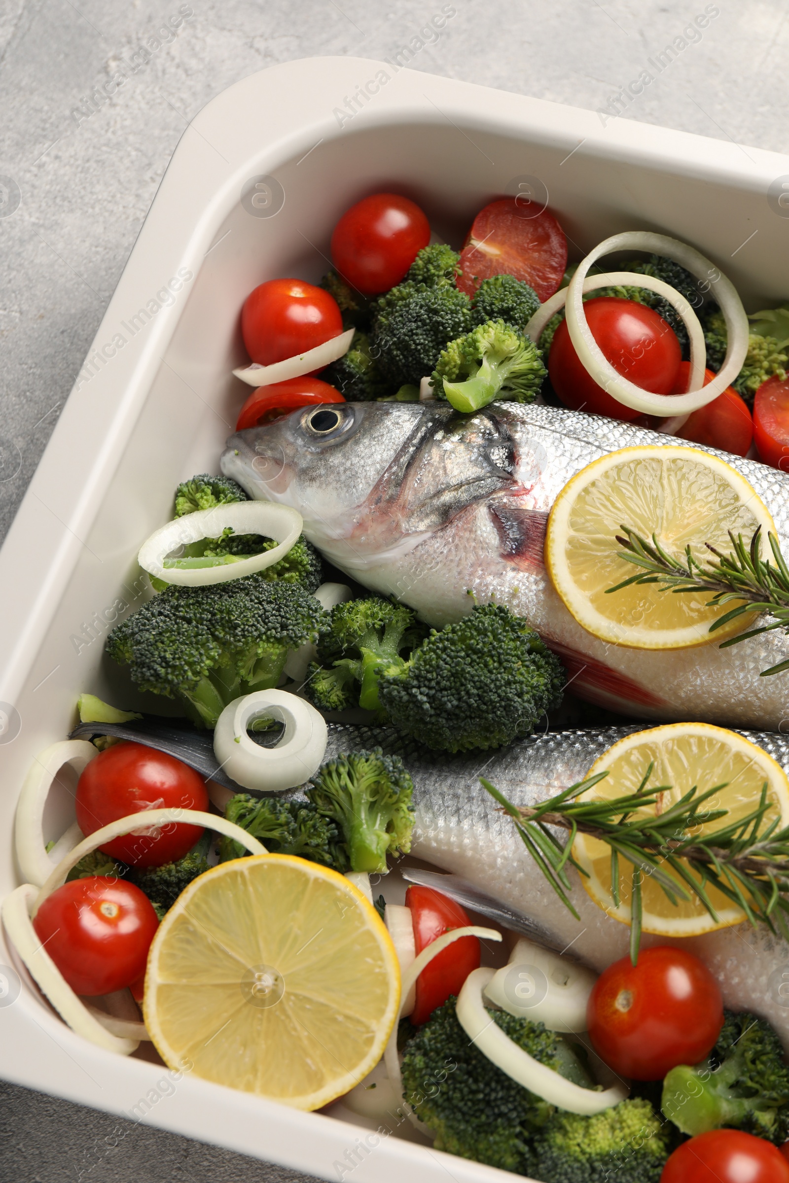 Photo of Raw fish with vegetables and lemon in baking dish on grey textured table, above view