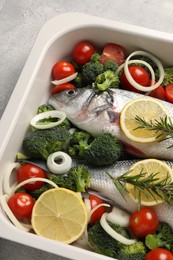 Photo of Raw fish with vegetables and lemon in baking dish on grey textured table, above view