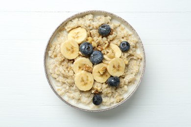 Tasty oatmeal with banana, blueberries, walnuts and honey served in bowl on white wooden table, top view