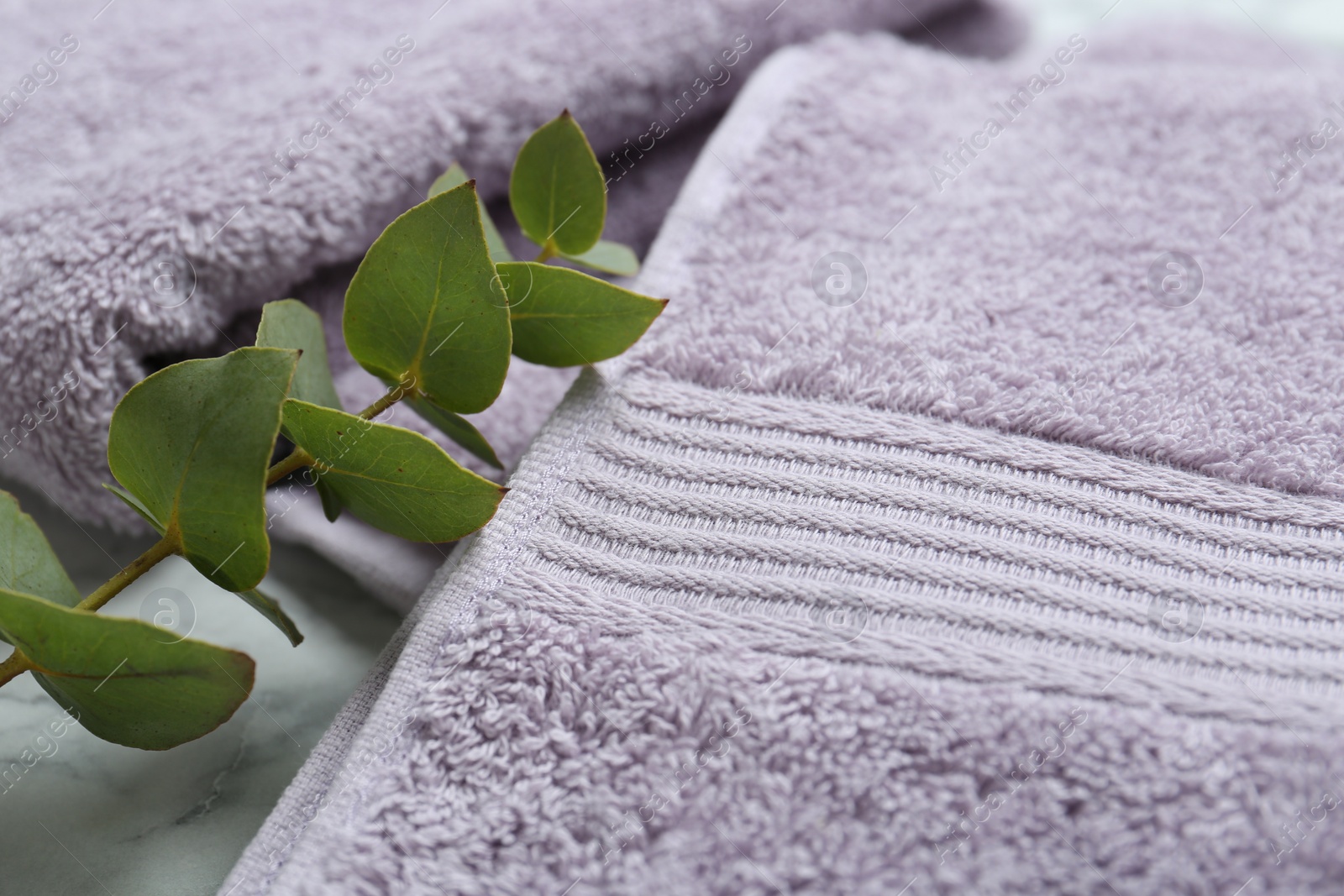 Photo of Violet terry towels and eucalyptus branch on table, closeup