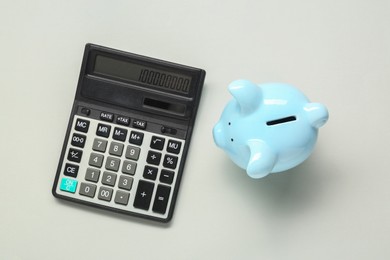 Calculator and piggy bank on light grey background, top view