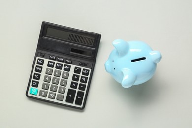 Photo of Calculator and piggy bank on light grey background, top view