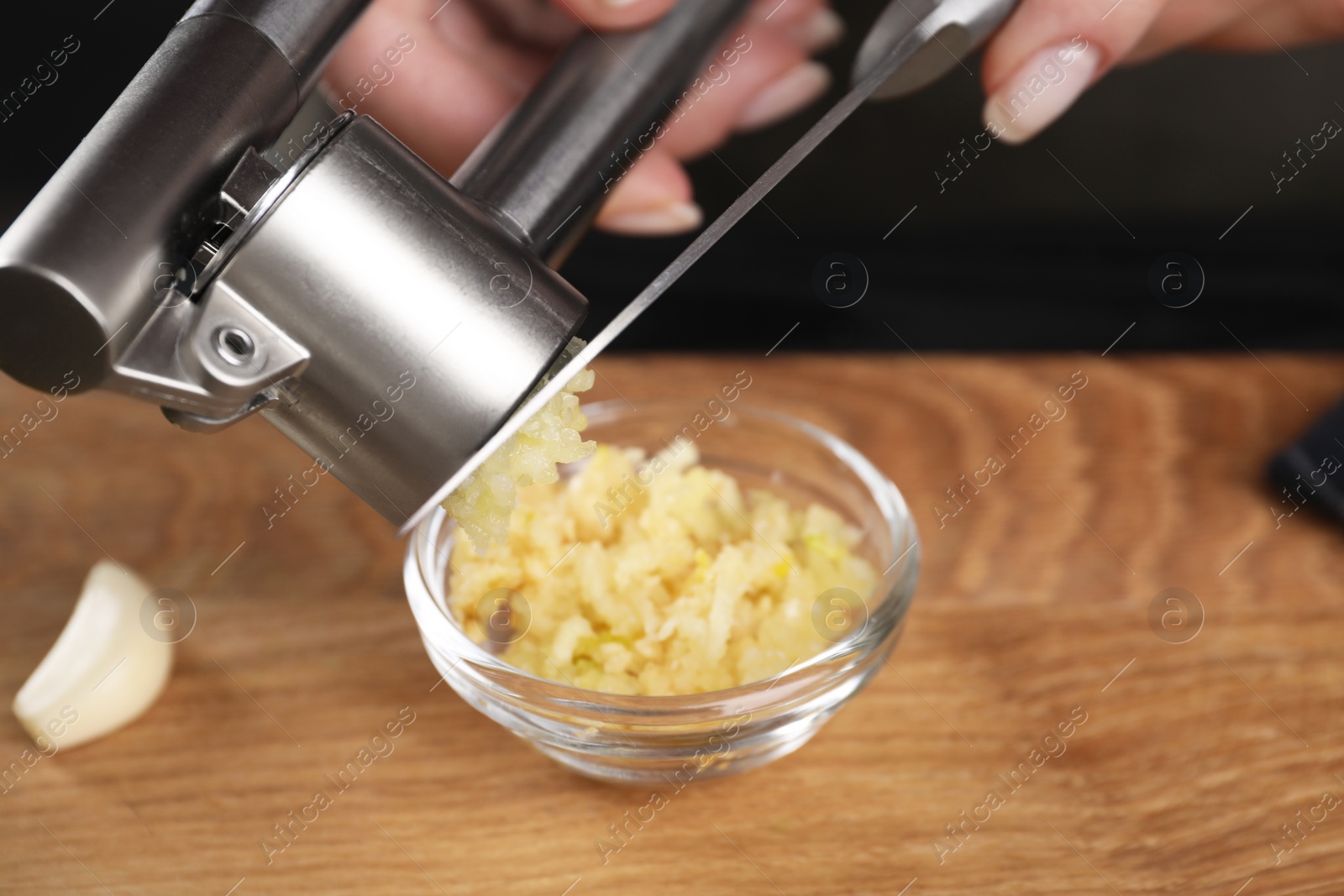 Photo of Woman squeezing garlic with press at wooden table, closeup