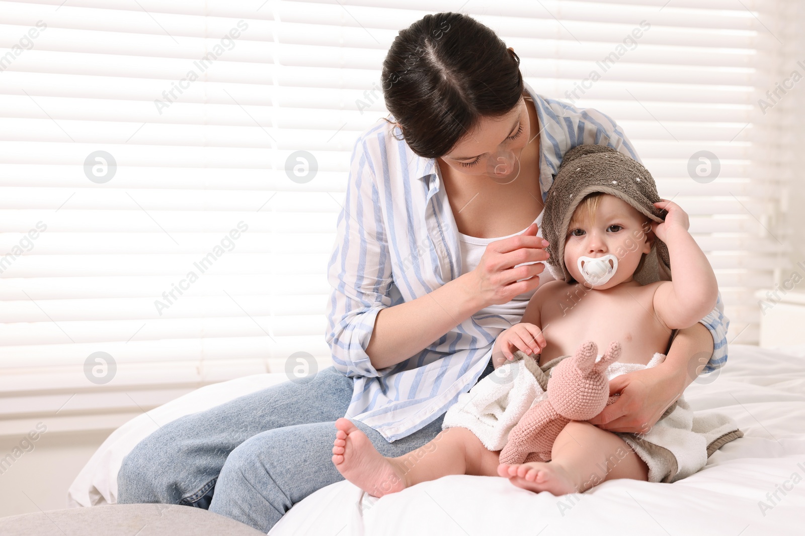 Photo of Mother wrapping her cute little baby with towel after bathing on bed