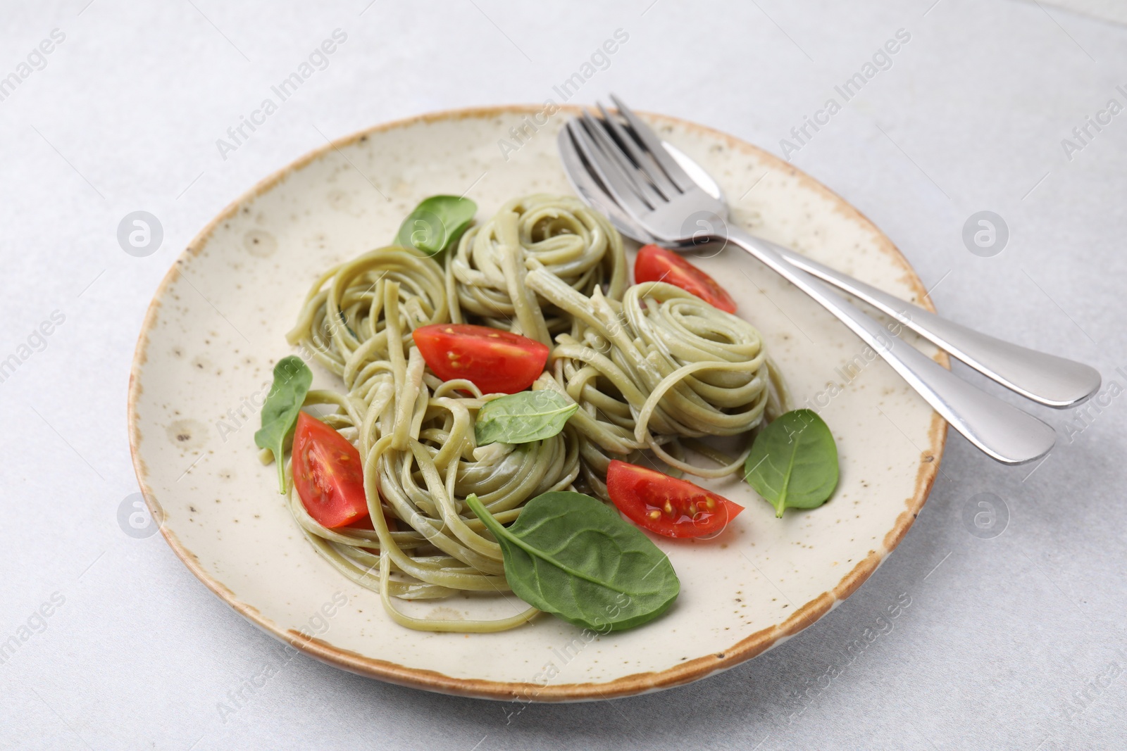 Photo of Tasty pasta with spinach, tomatoes and cutlery on light grey table