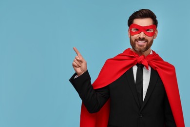 Photo of Businessman wearing red superhero cape and mask on light blue background. Space for text