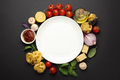 Plate surrounded by different types of pasta and products on black background, flat lay. Space for text