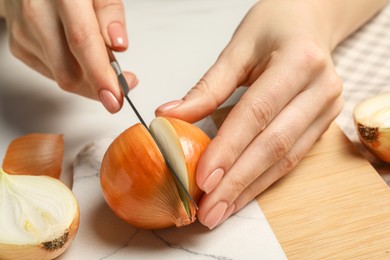 Woman cutting ripe onion at white table, closeup