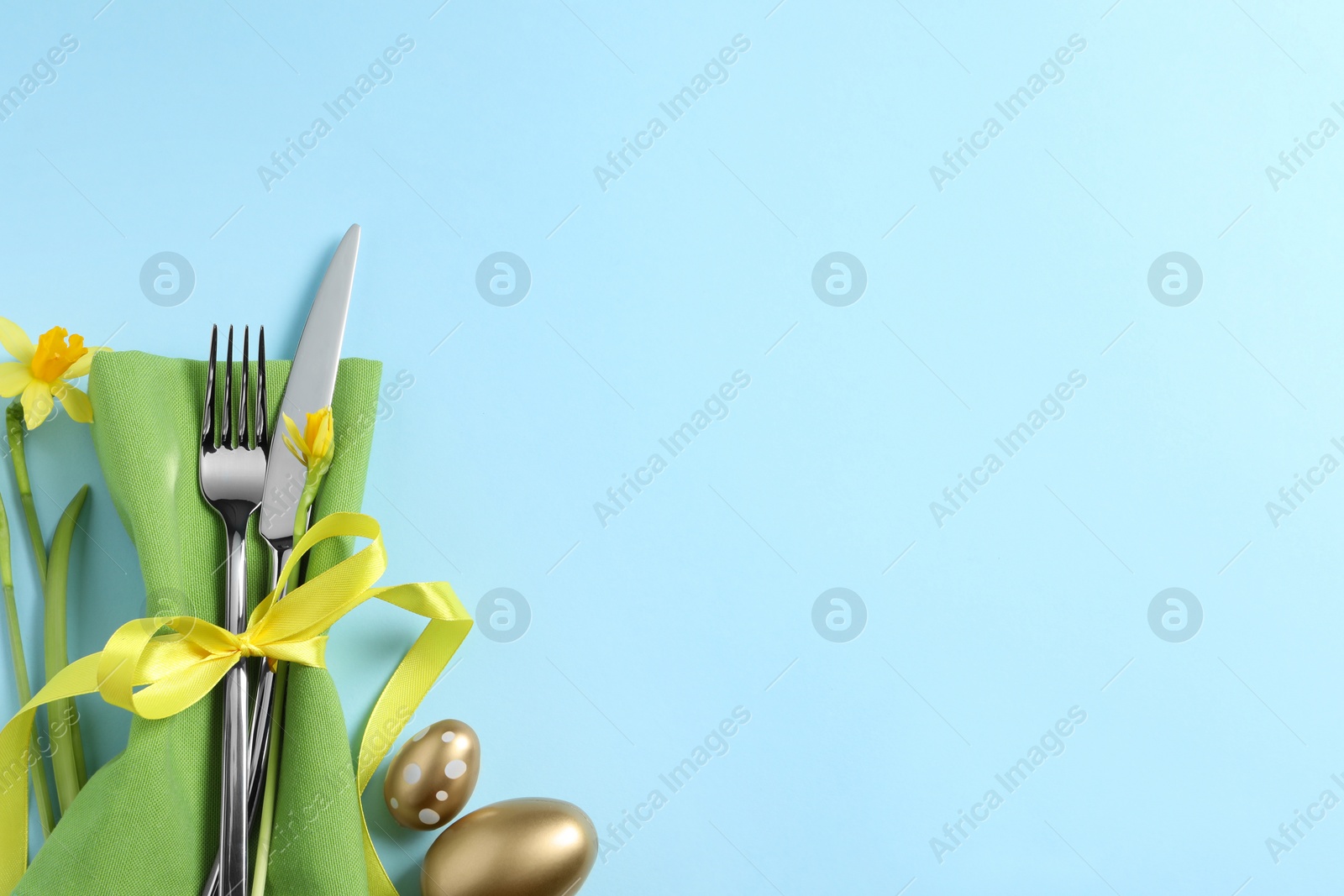 Photo of Cutlery set, Easter eggs and narcissuses on light blue background, flat lay with space for text. Festive table setting