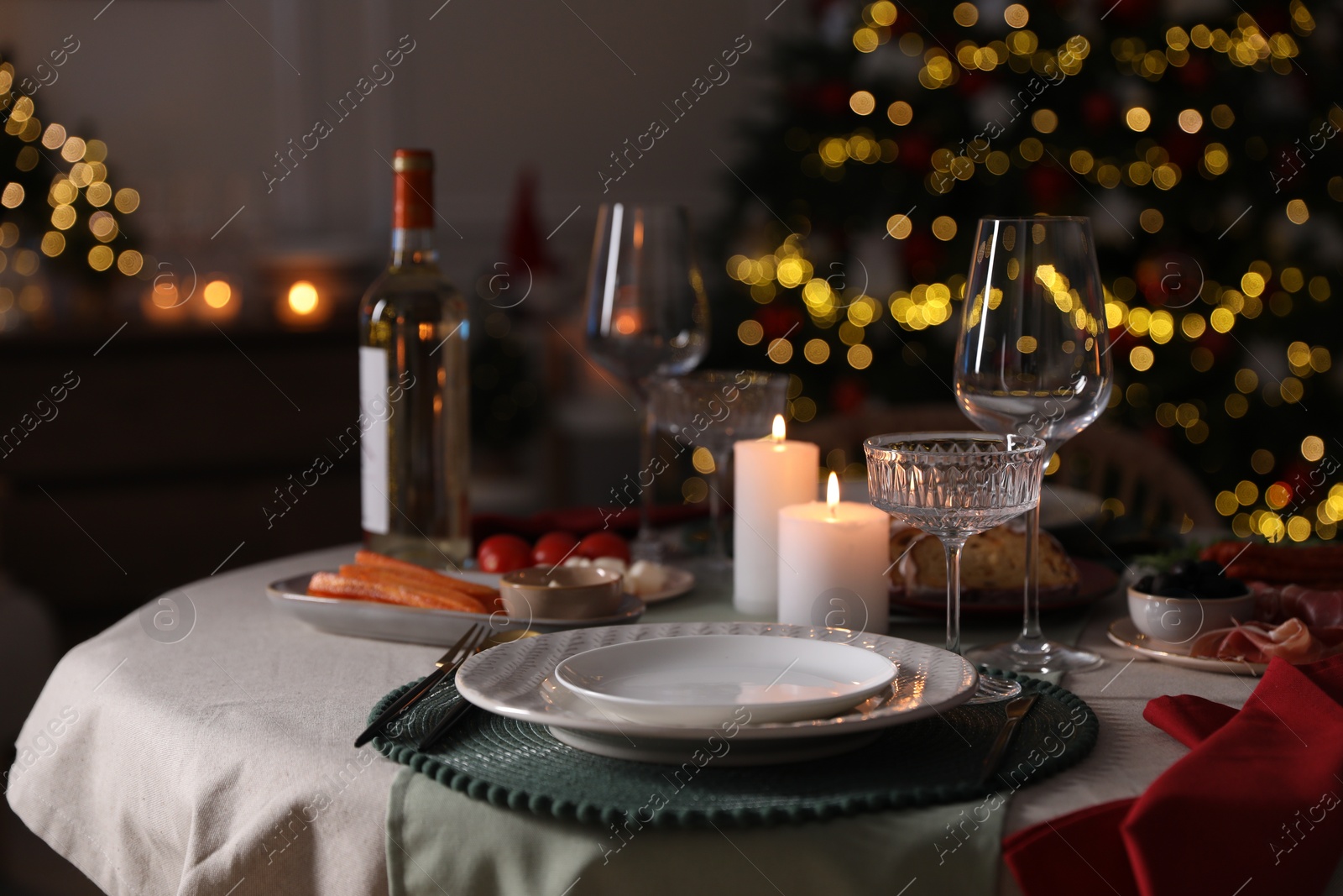 Photo of Christmas table setting with burning candles, appetizers and dishware indoors