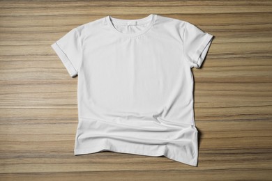 Stylish white T-shirt on wooden table, top view