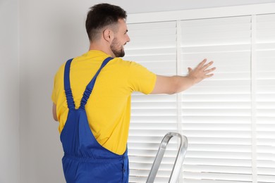 Worker in uniform installing horizontal window blinds indoors