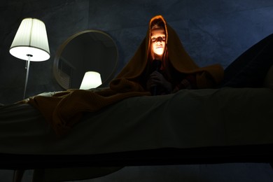 Photo of Little girl with flashlight in blanket on sofa at night, low angle view