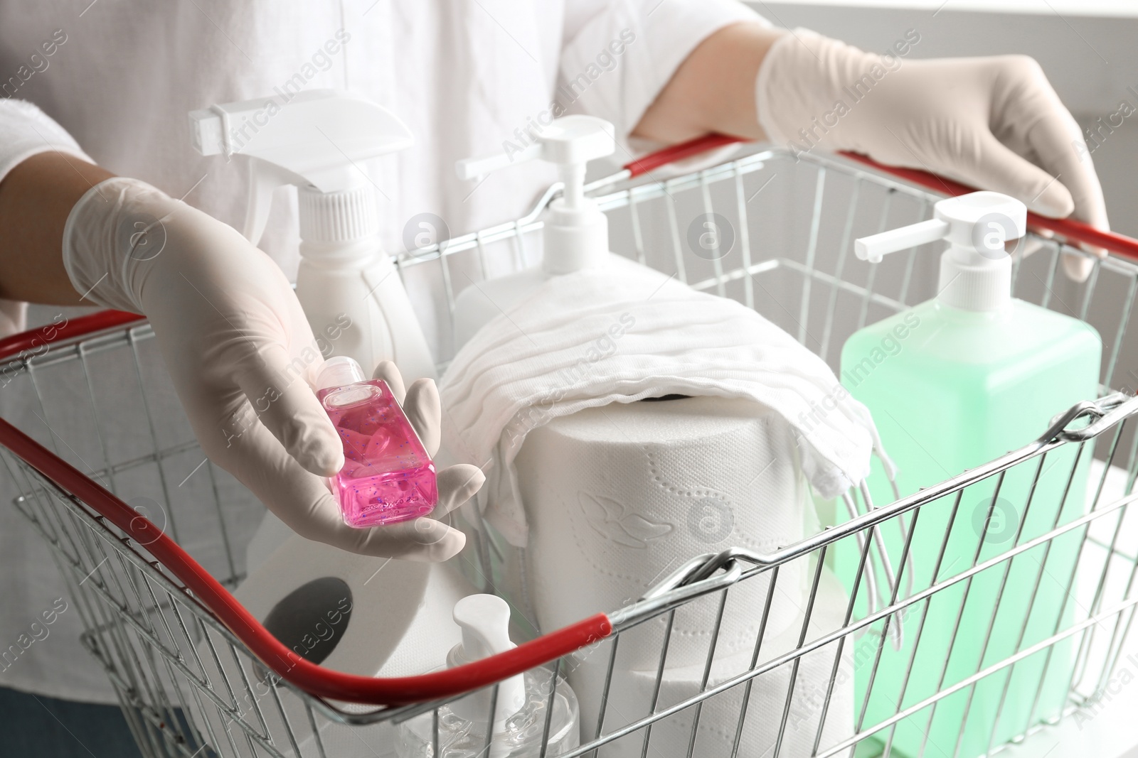 Photo of Woman with shopping basket full of antiseptics and toilet paper, closeup. Panic caused by virus