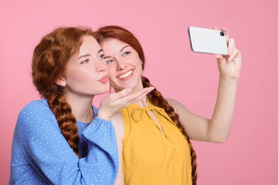 Beautiful young redhead sisters taking selfie on pink background