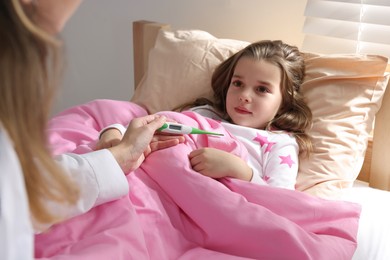Photo of Doctor with thermometer near little girl in bed indoors
