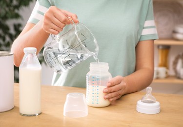 Photo of Woman preparing infant formula at table indoors, closeup. Baby milk