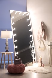 Photo of Large mirror with light bulbs and knitted pouf in stylish room. Interior design