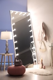 Large mirror with light bulbs and knitted pouf in stylish room. Interior design